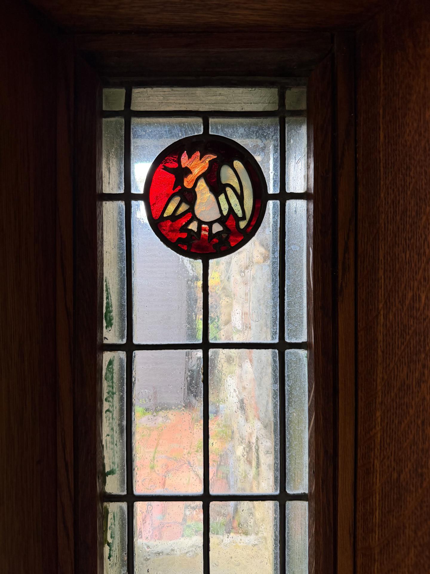 Stained-glass window with a red circular bird design in a dark wooden door