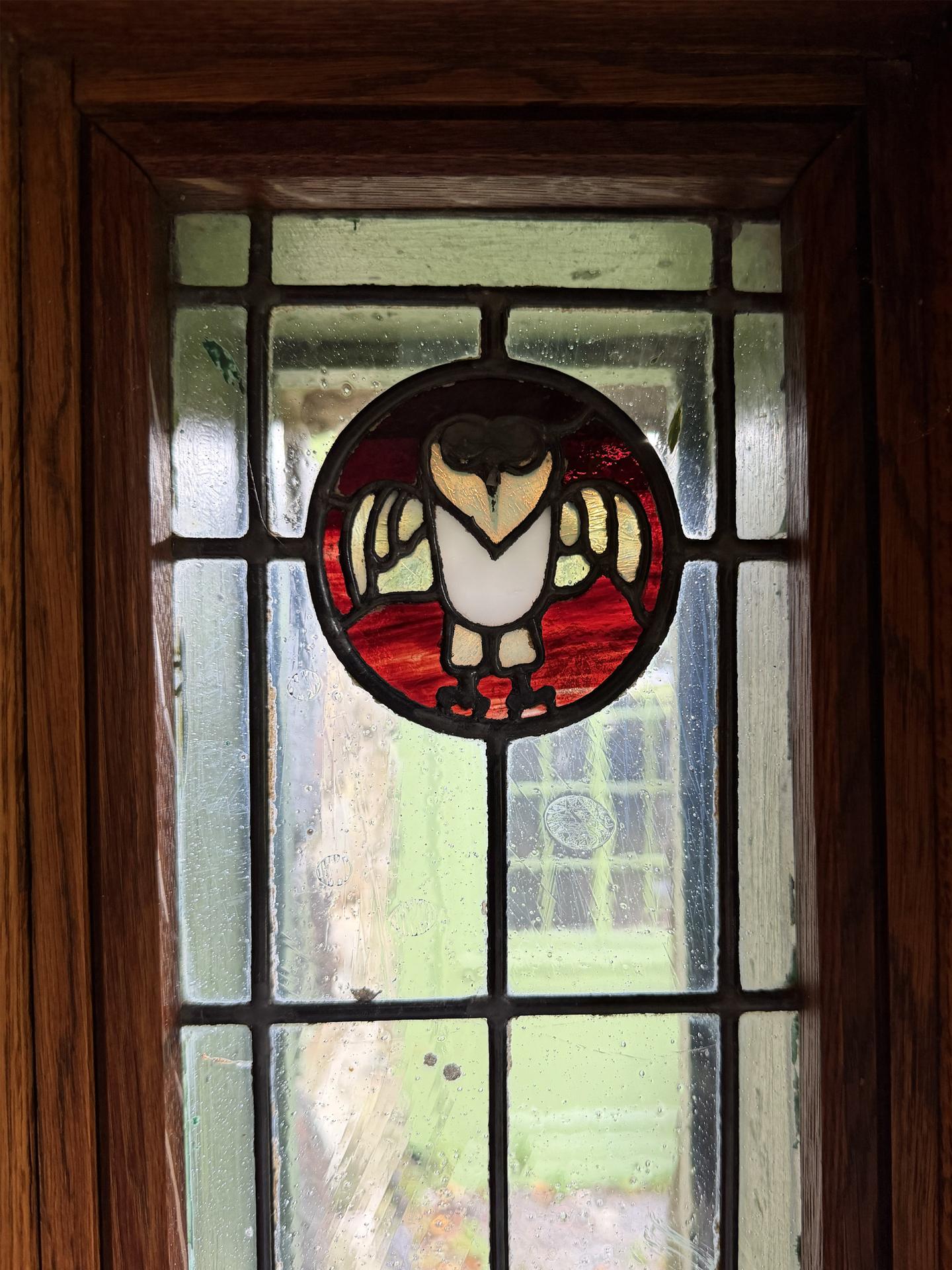 Stained-glass owl medallion in a dark wooden window frame
