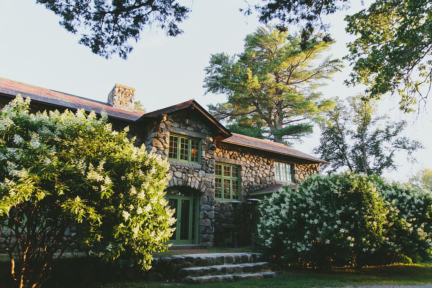 Rustic wooden house surrounded by lush trees and shrubs.