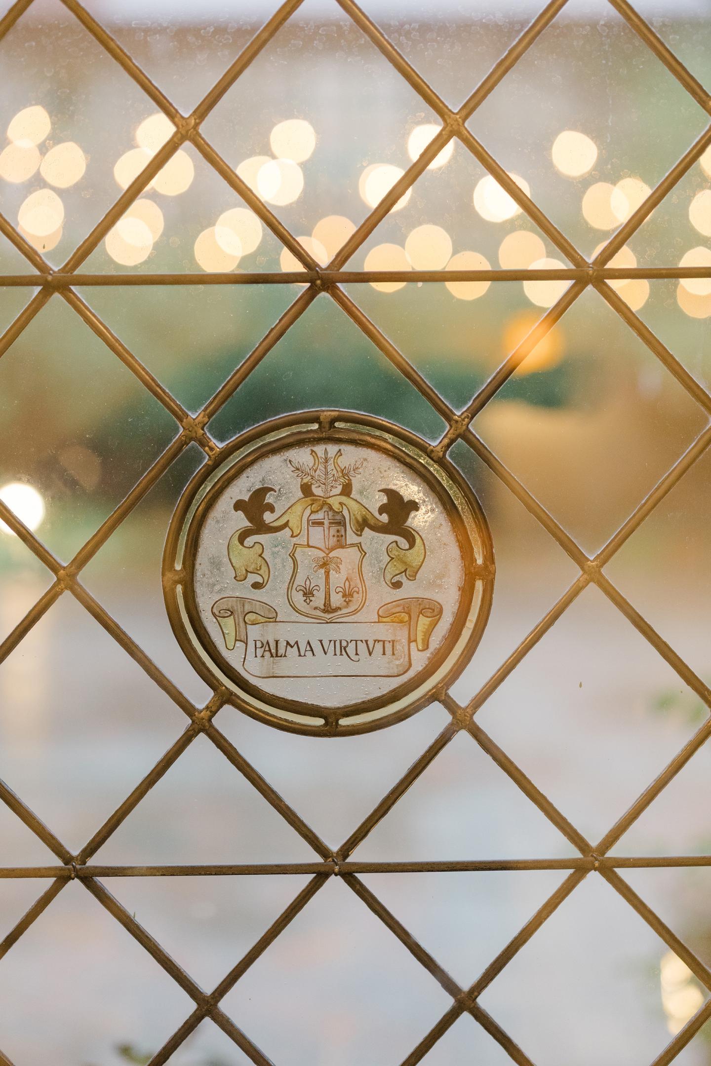 Ornate gold emblem on a diamond-patterned glass window with blurred lights behind