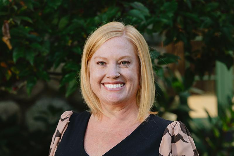 Portrait of a smiling blonde woman in a black blouse outdoors.