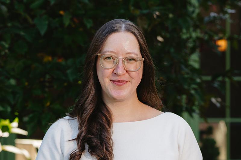 Portrait of a smiling woman with glasses and long brown hair outdoors.